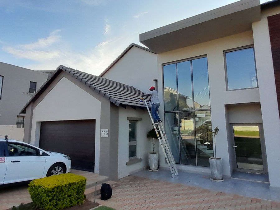 A technician on a ladder at a modern double-storey house, a branded car in the driveway