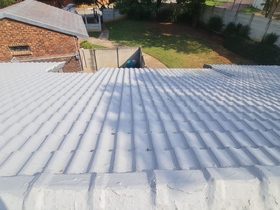 A pitched cement tiled roof, seen from the ridge over a garden
