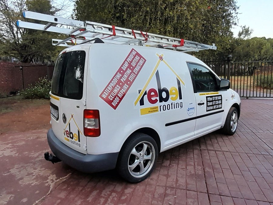 A white Rebel Roofing branded van with ladders on its roof rack